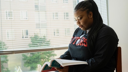 Black female student sitting by dorm window reading