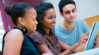 3 person group, two black women, one poc male looking at a document together