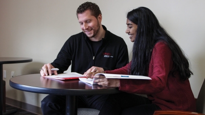 One male worker assisting a POC long haired female student, both examining papers on the table