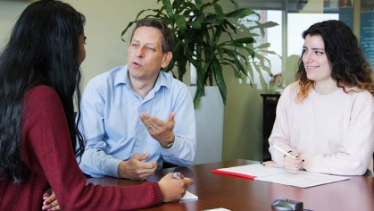 3 people sitting around a table, middle male talking, 2 female students