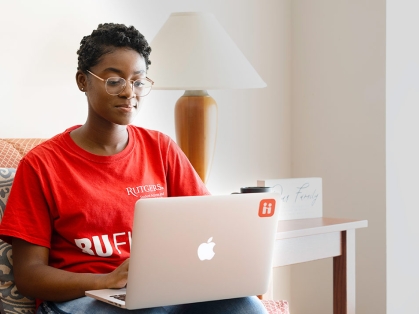 Rutgers black student with red RU shirt and glasses sitting inside with a laptop