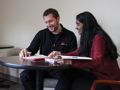 One male worker assisting a POC long haired female student, both examining papers on the table